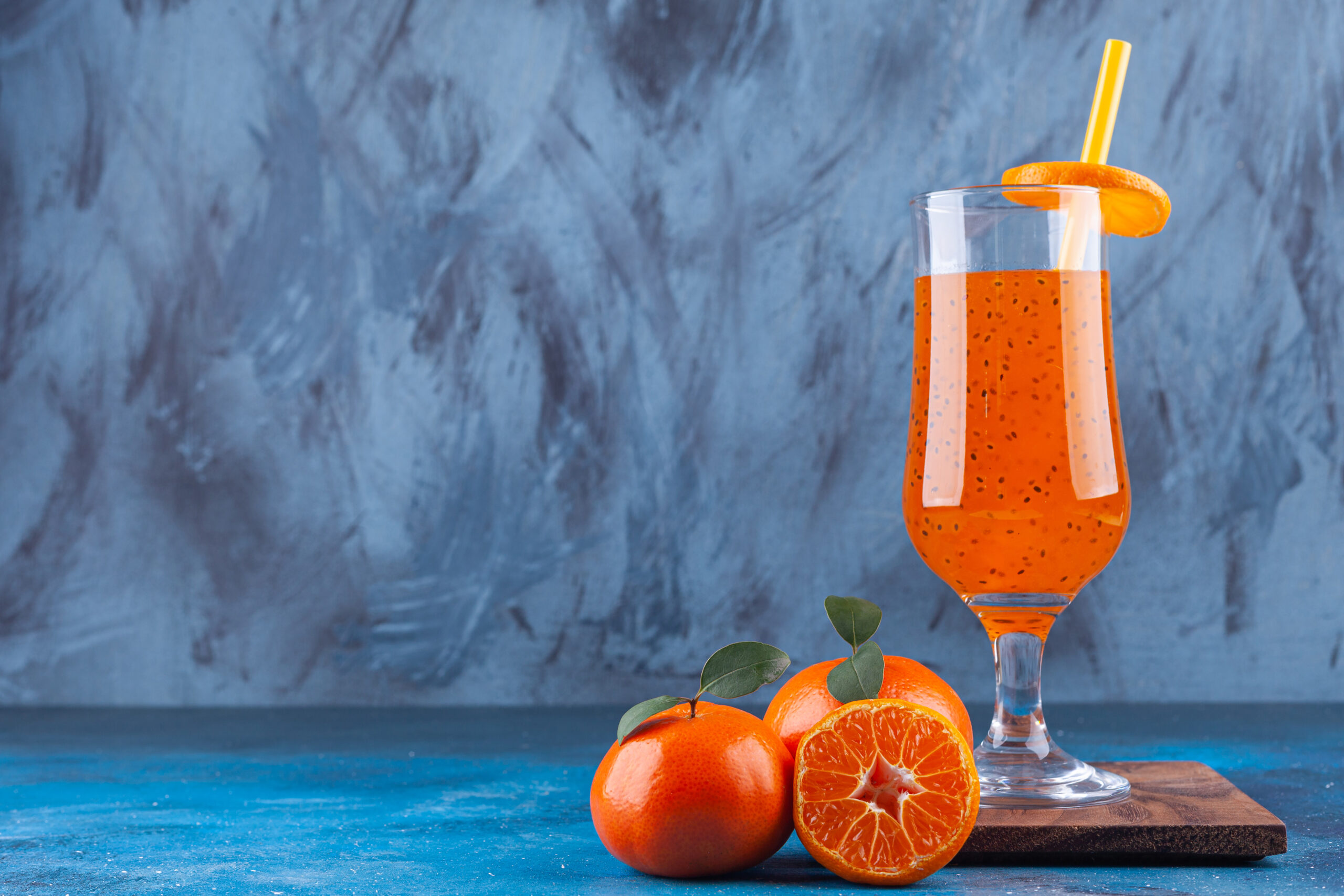 A glass cup of juice with straw and whole and sliced tangerines. High quality photo